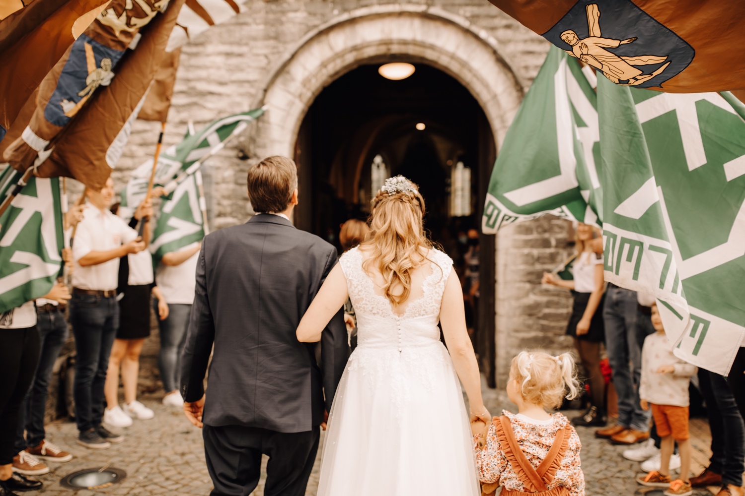 bruid wandelt met vader de kerk van belsele binnen door vlaggen van de jeugdbeweging