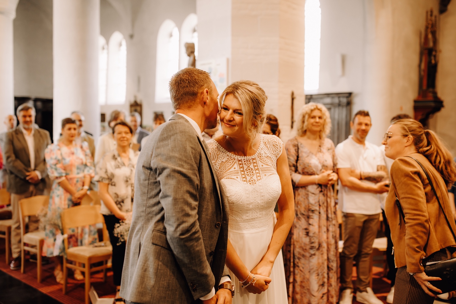 bruidegom fluistert iets in het oor van de bruid in de kerk van Meldert