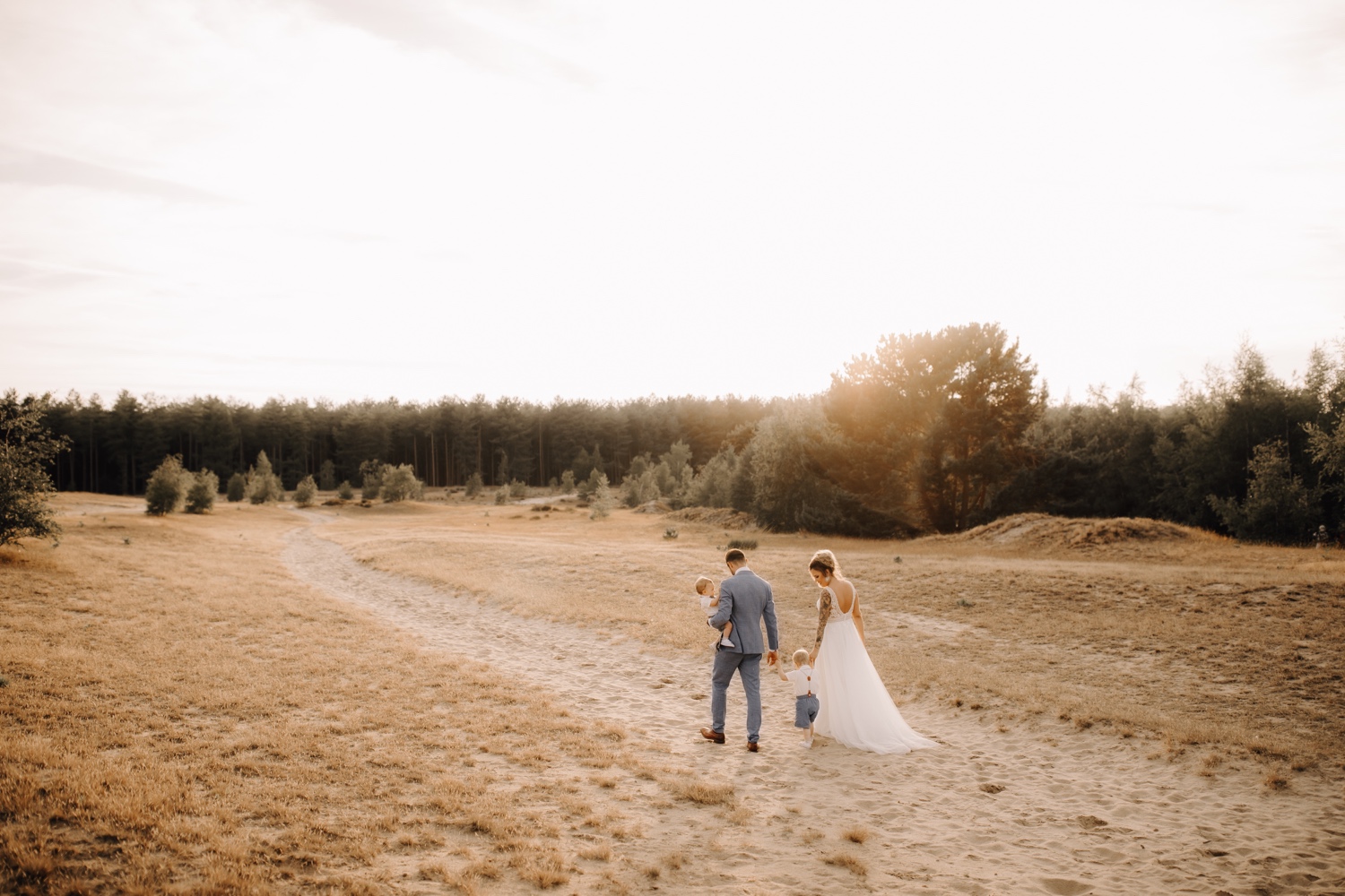 Huwelijksfotograaf Limburg - bruidspaar wandelt door veld samen met hun kinderen bij zonsondergang