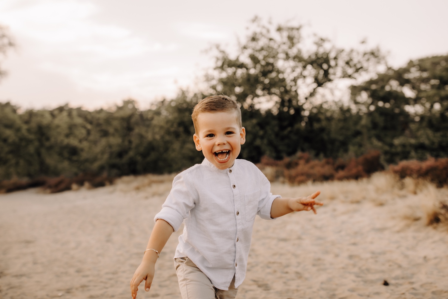 gezinsfotograaf Limburg - zoontje loopt richting camera met een grote lach op zijn gezicht