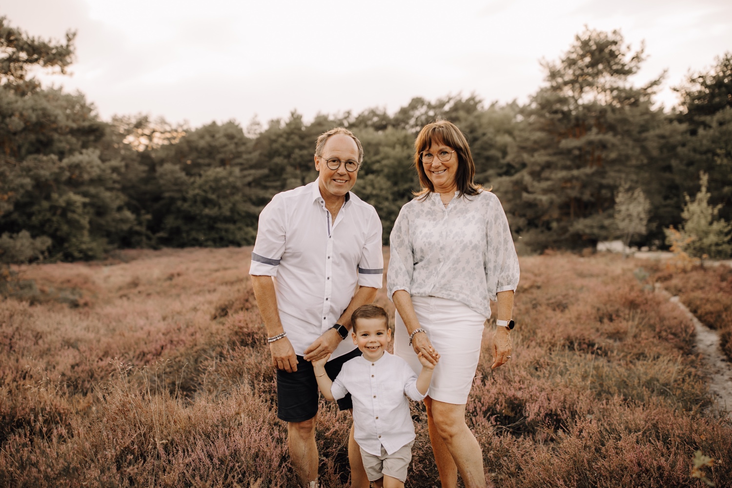 gezinsfotograaf Limburg - oma en opa poseren met kleinzoon voor de camera tussen de heide van Zonhoven