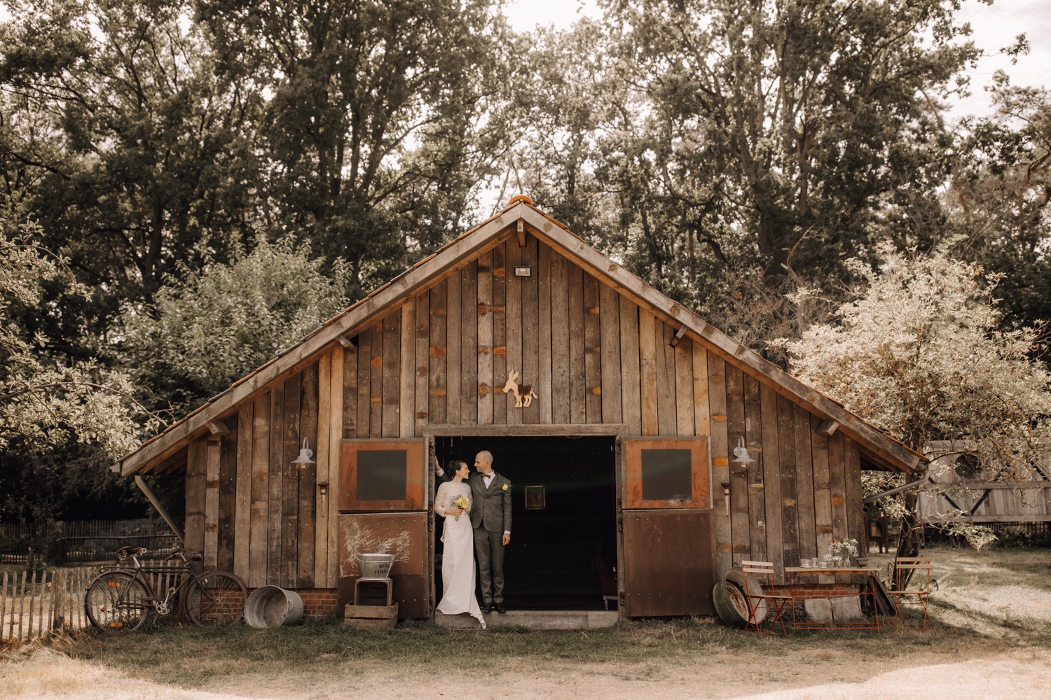 Huwelijksfotograaf Limburg - bruidspaar poseert in deuropening van de schuur bij ferme neelke