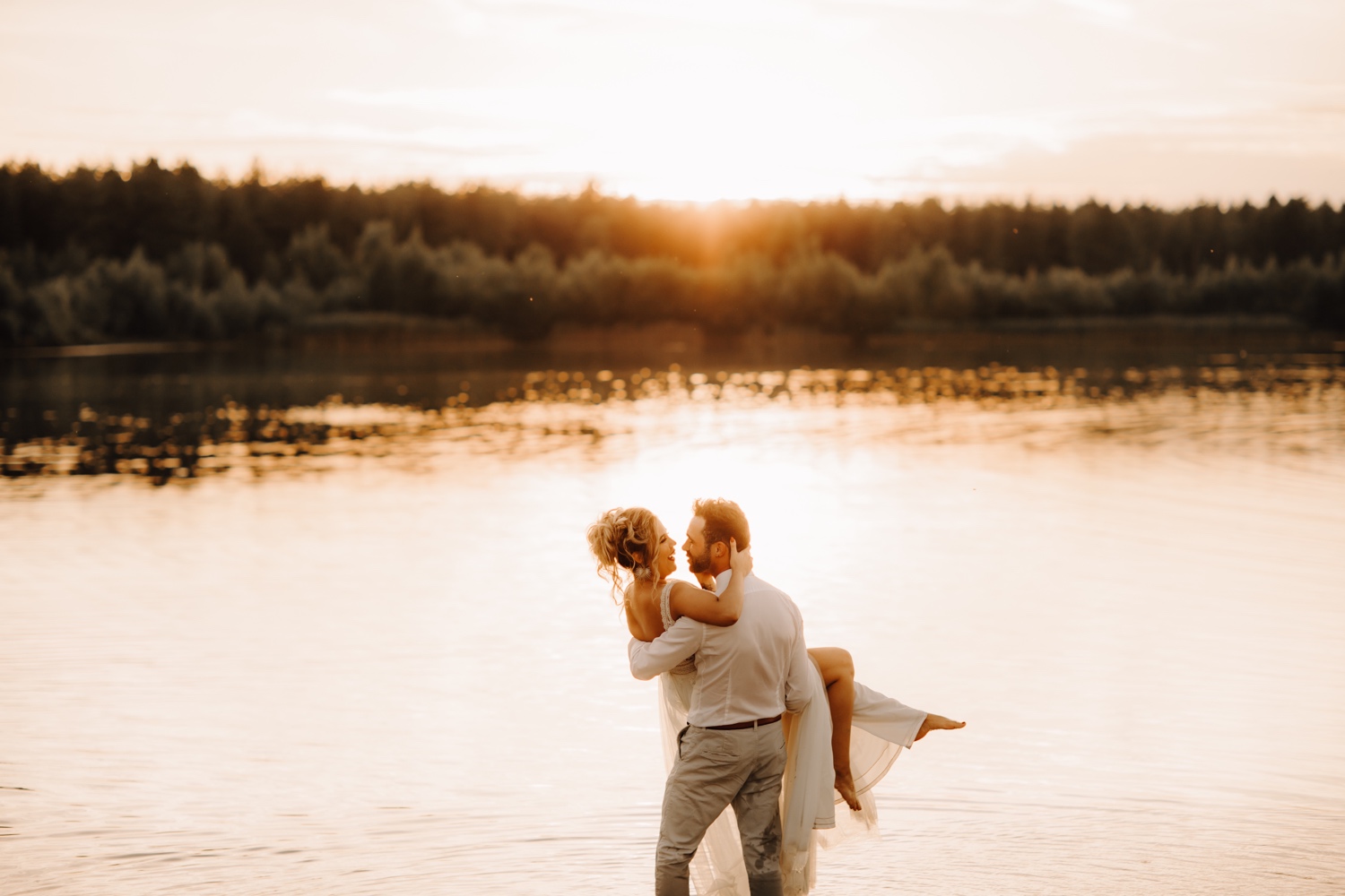 Huwelijksfotograaf Limburg - bruidegom heft zijn bruid op in water tijdens zonsondergang