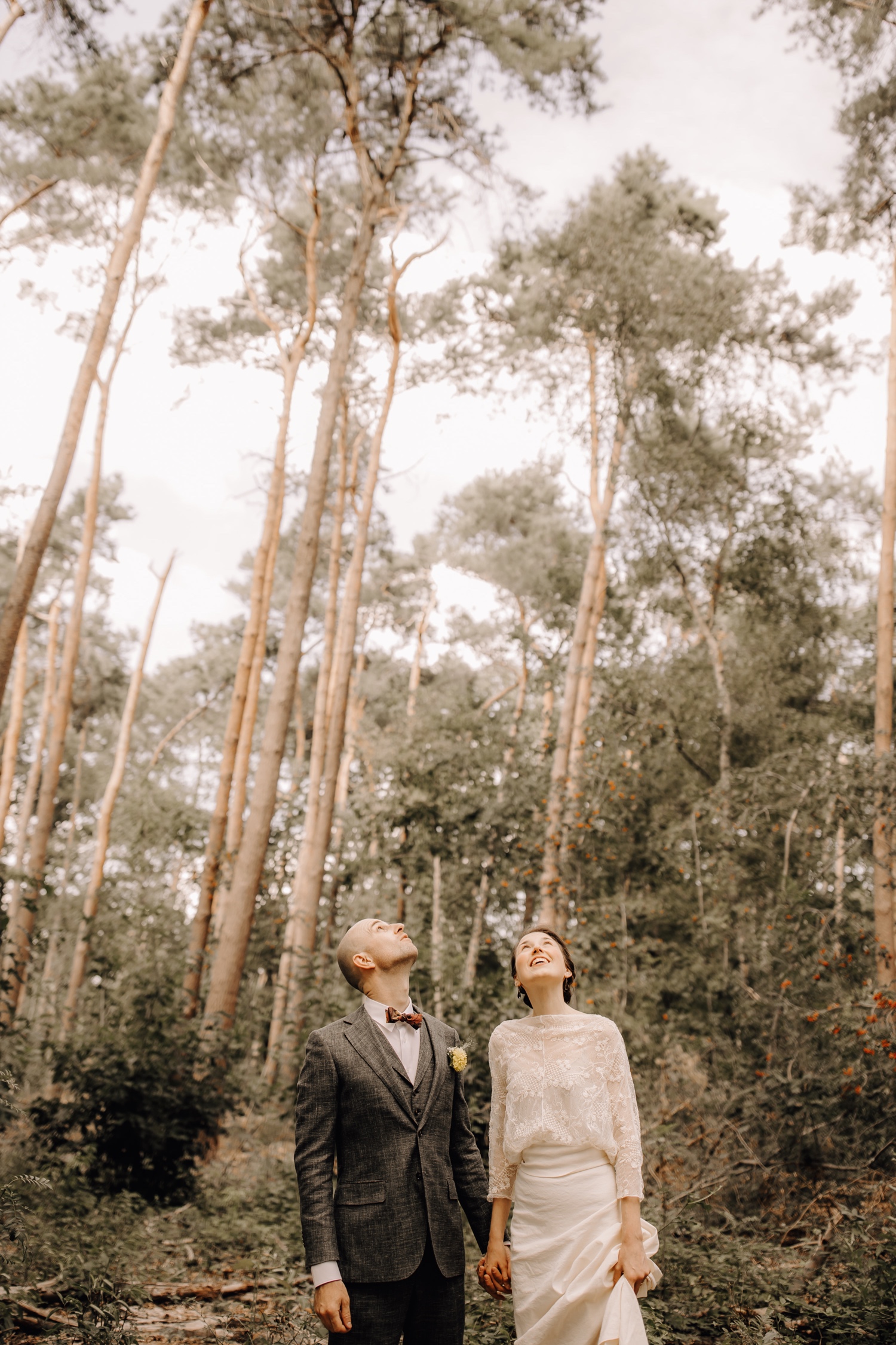 Huwelijksfotograaf Limburg - bruidspaar kijkt naar boven tussen de hoge bomen