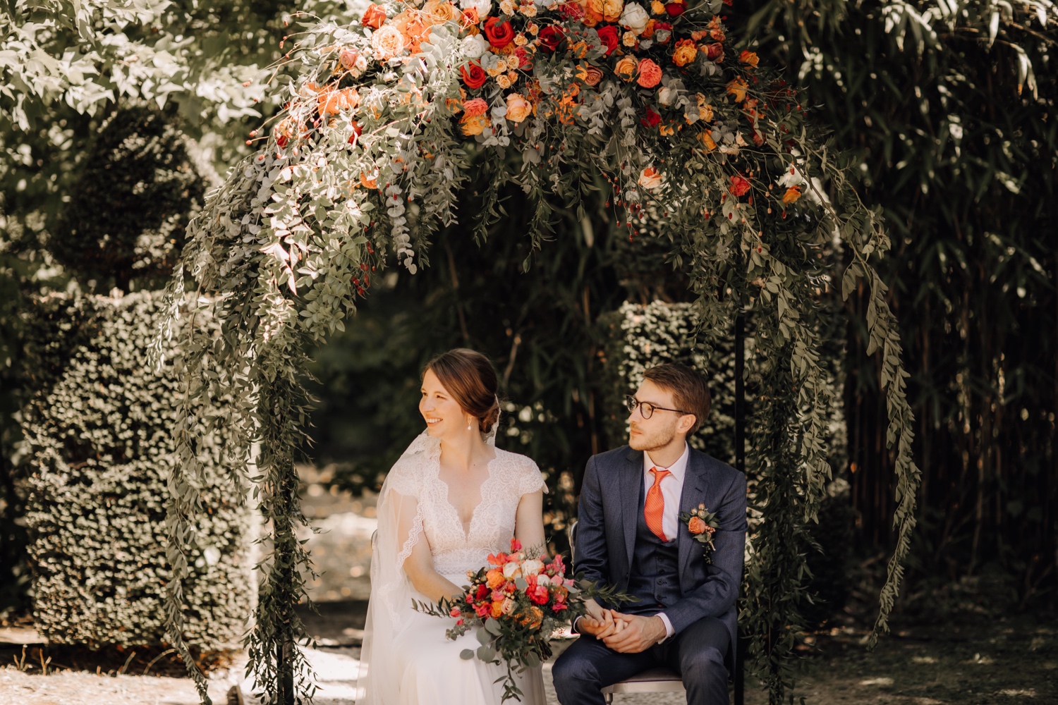 Huwelijksfotograaf Limburg - bruidspaar zit onder bloemenboog tijdens ceremonie