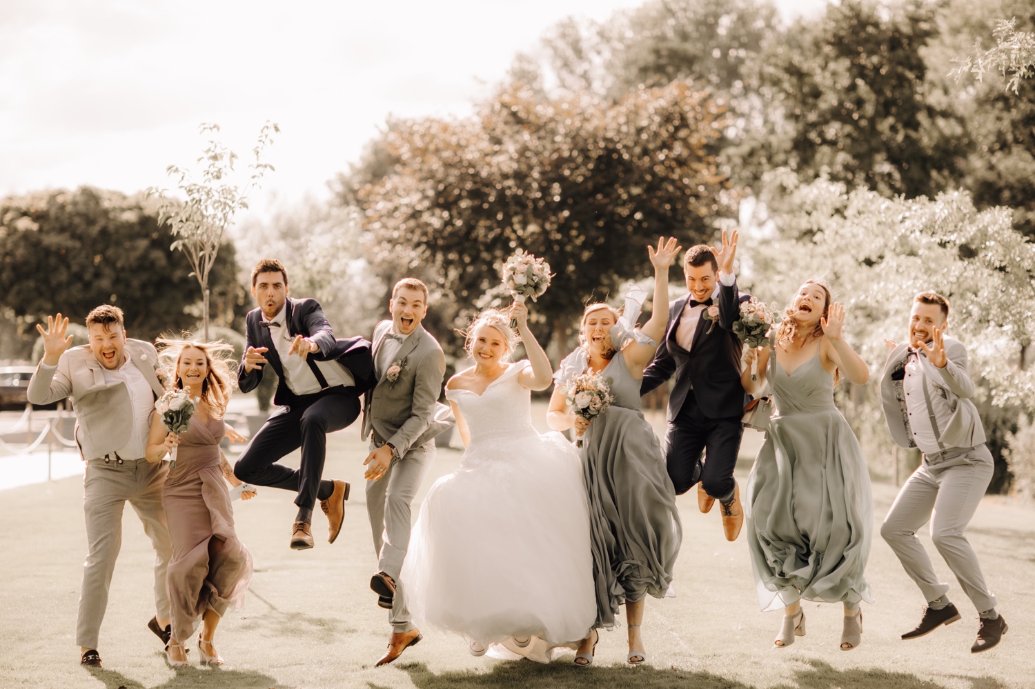 Huwelijksfotograaf Limburg - bruidspaar en vrienden springen in de lucht voor groepsfoto