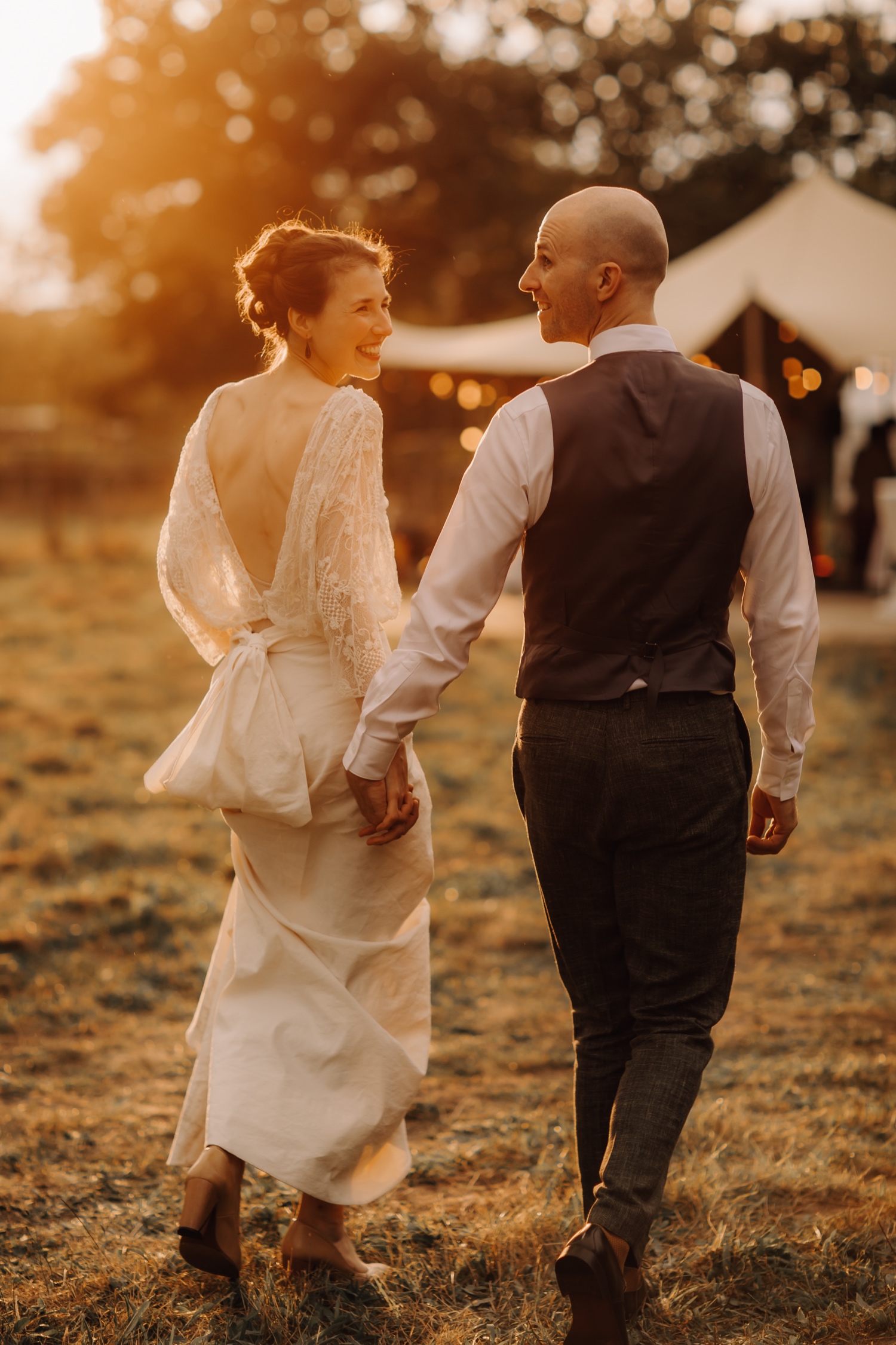 Huwelijksfotograaf Limburg - bruidspaar wandelt richting tent tijdens zonsondergang