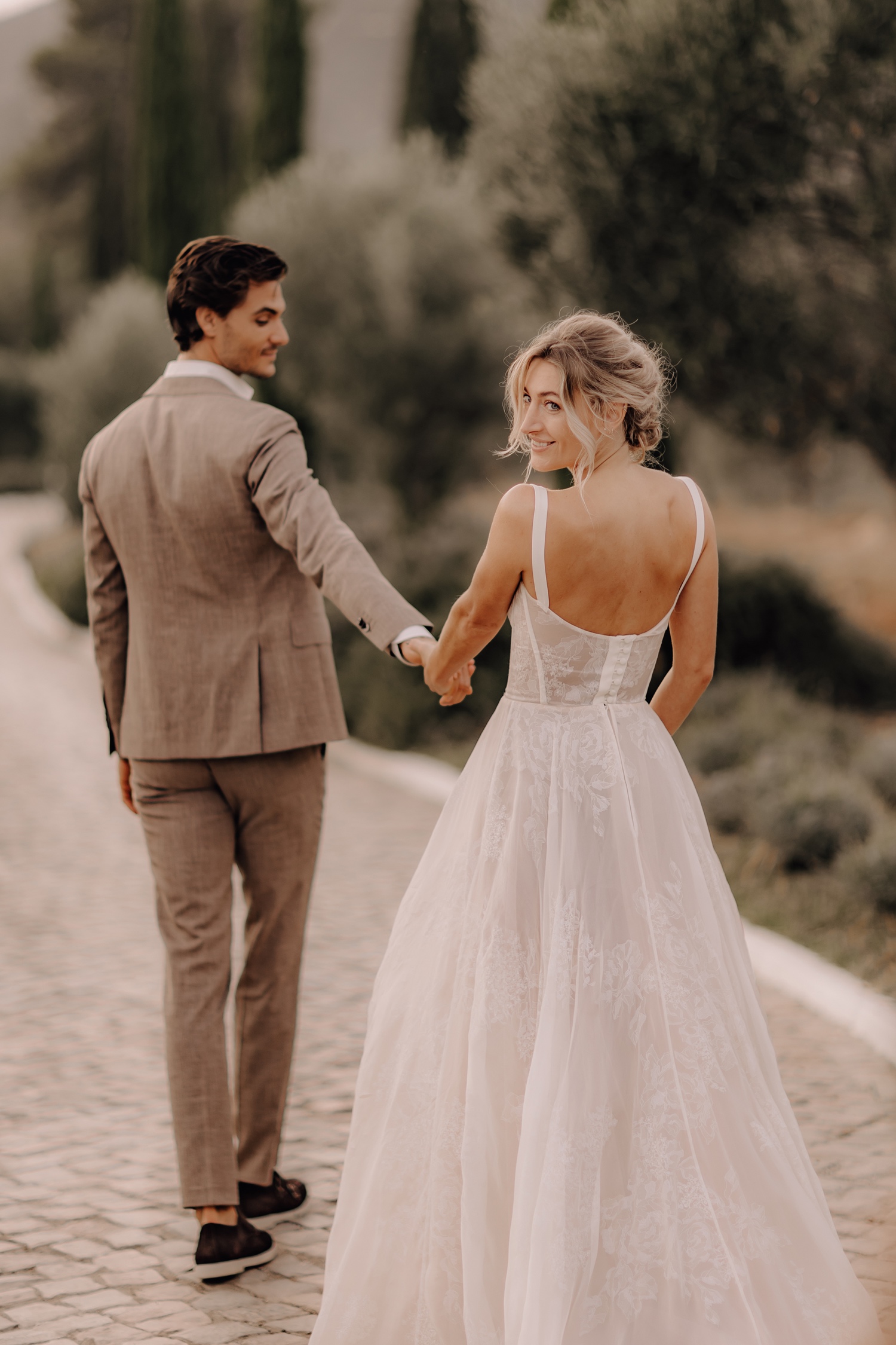 Huwelijksfotograaf buitenland - bruidspaar wandelt tussen de cipressen in Portugal