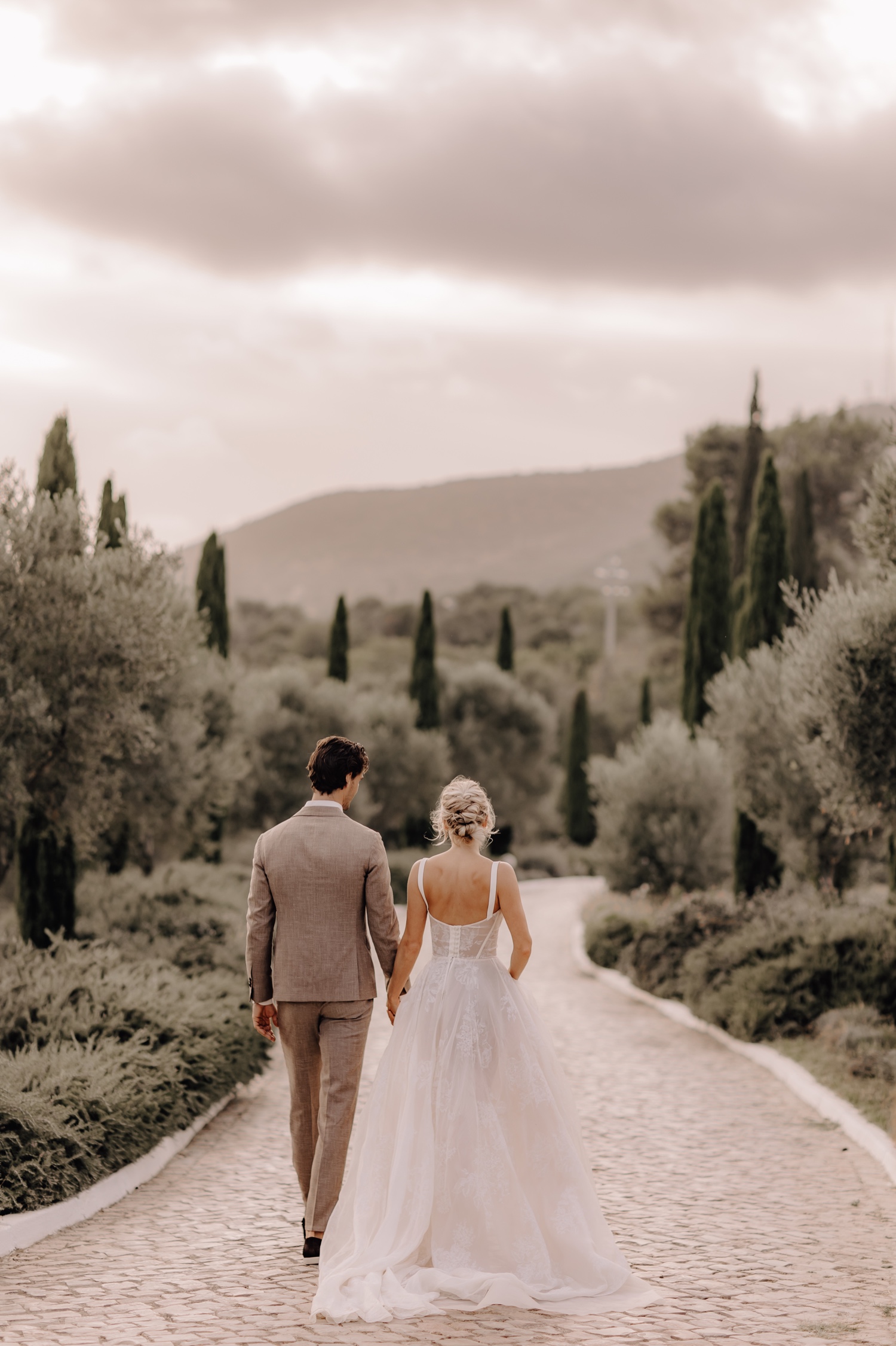 Huwelijksfotograaf buitenland - bruidspaar wandelt weg tussen de cipressen in Portugal