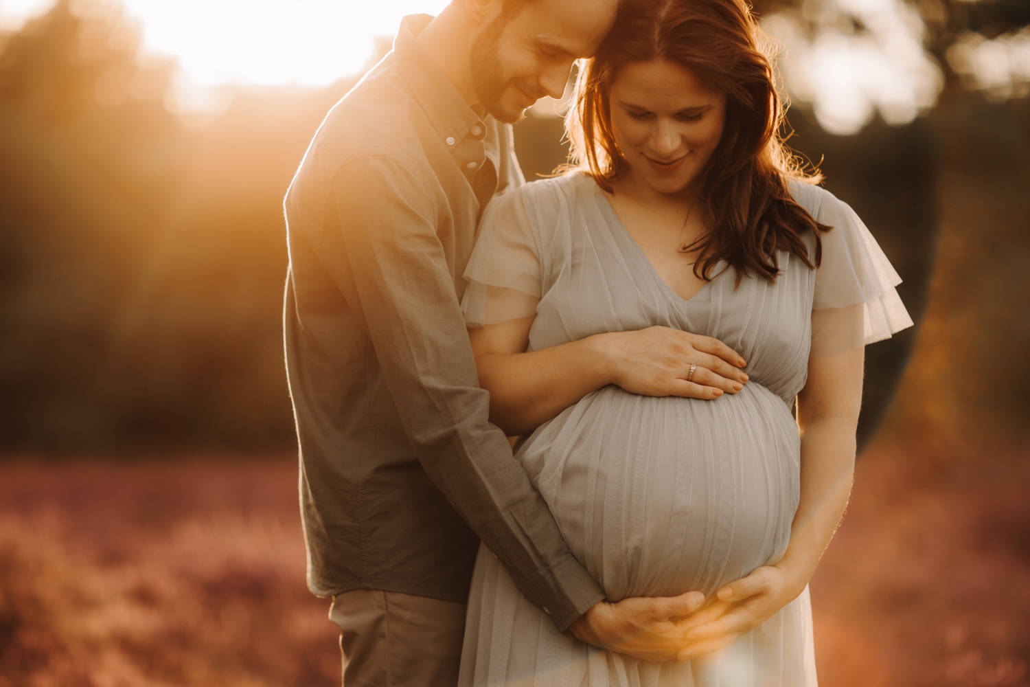 gezinsfotograaf Limburg - koppel kijkt naar zwangere buik tijdens fotoshoot in de teut van Zonhoven