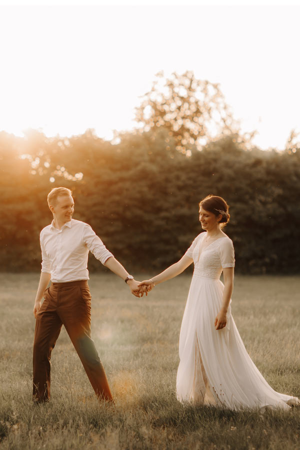 Huwelijksfotograaf Limburg - bruidspaar wandelt door de velden tijdens zonsondergang