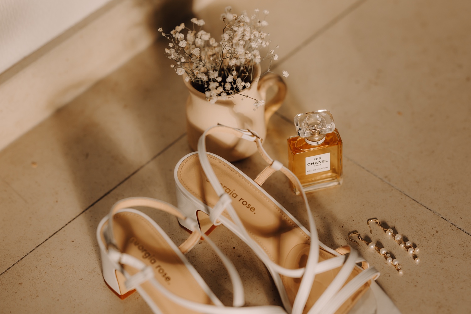 detailfoto van de schoenen, parfum en oorbellen van de bruid