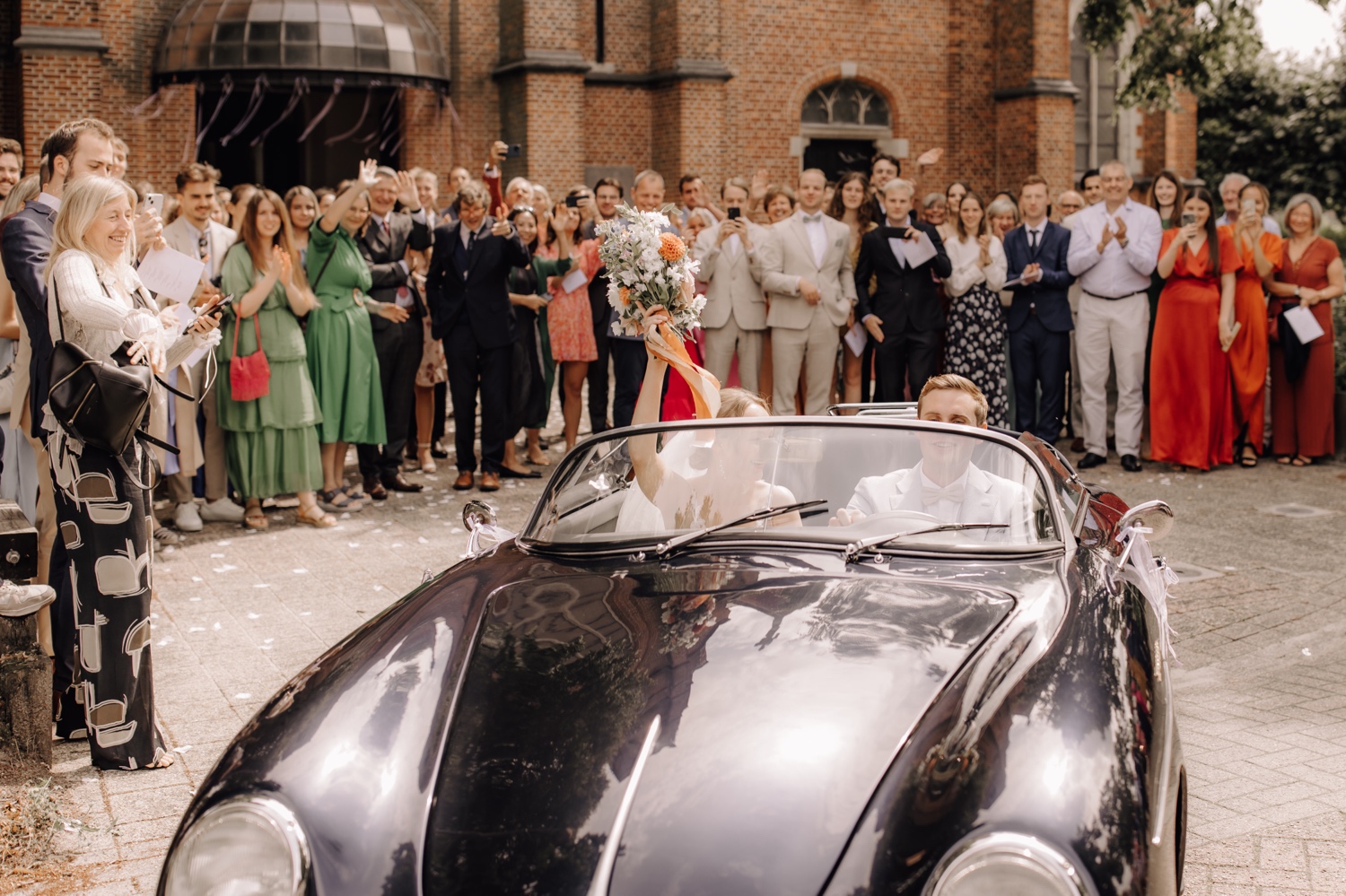 bruidspaar rijdt weg in oldtimer Porsche