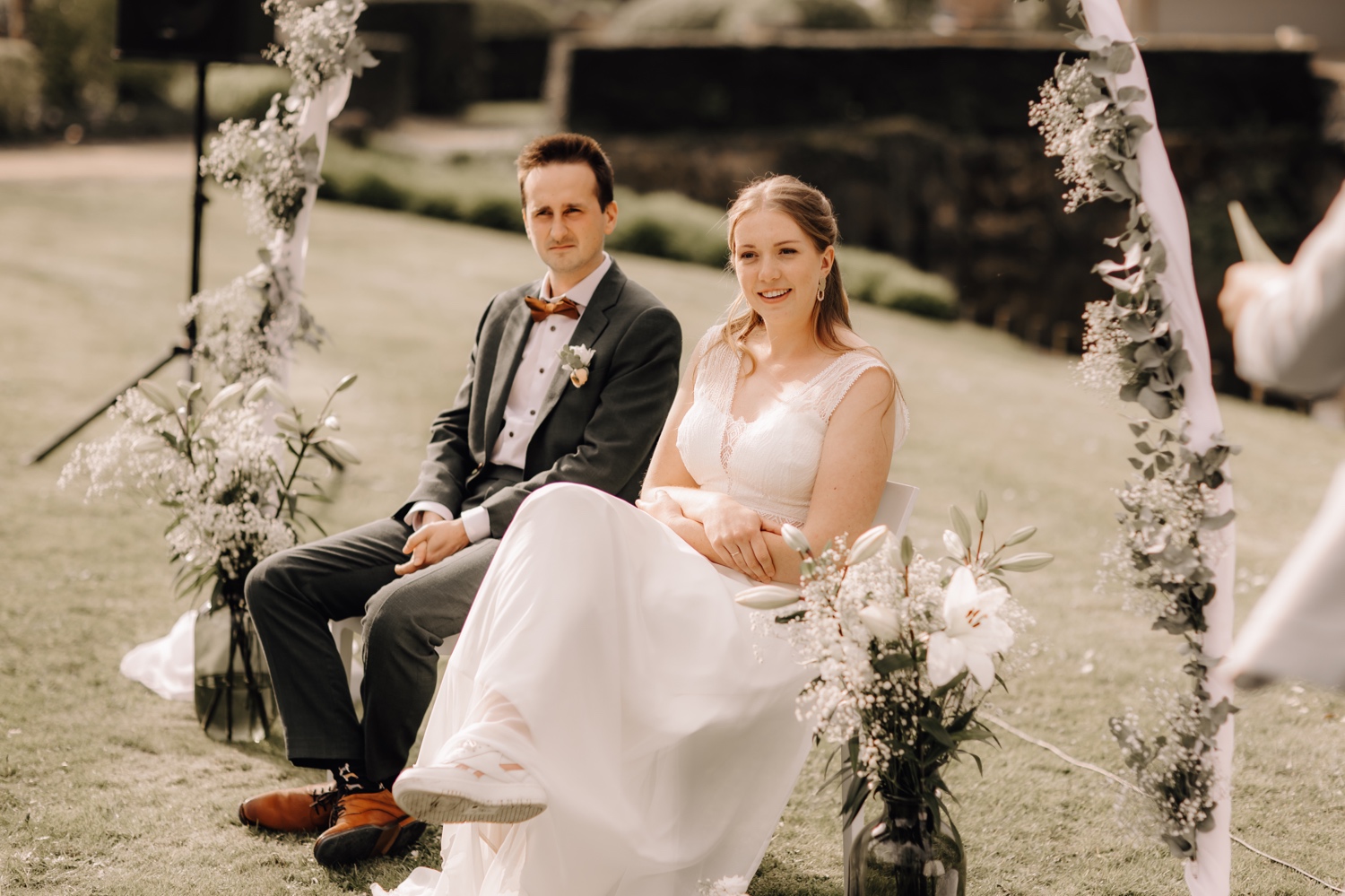 Huwelijksfotograaf Limburg - bruidspaar zit onder een bloemenboog tijdens de ceremonie