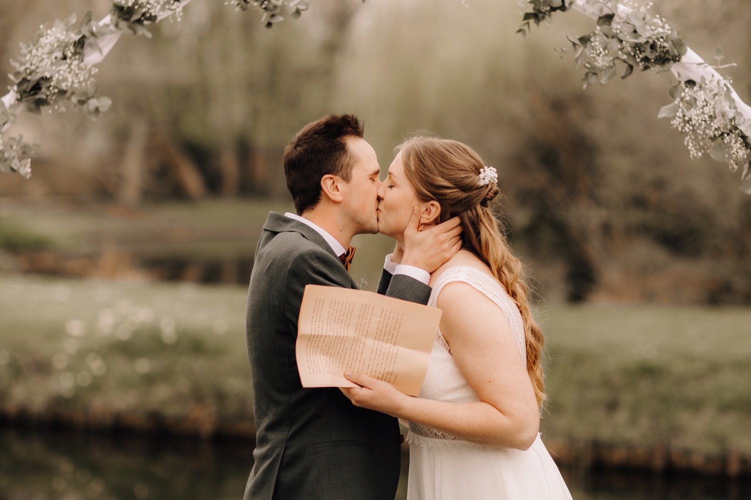 Huwelijksfotograaf Limburg - bruidspaar kust elkaar onder bloemenboog