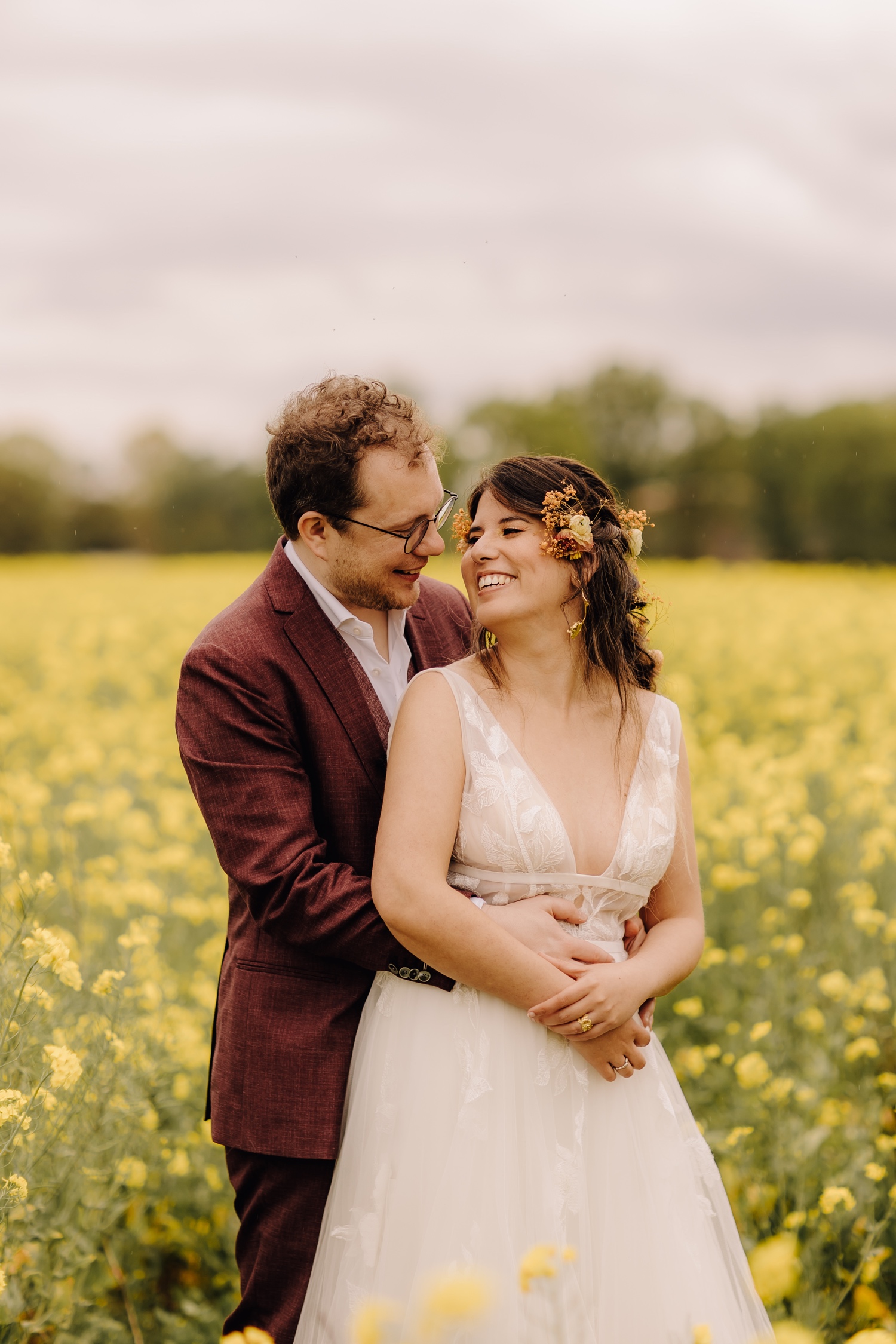 Huwelijksfotograaf Limburg - bruidspaar kijkt naar elkaar te midden van een koolzaadveld