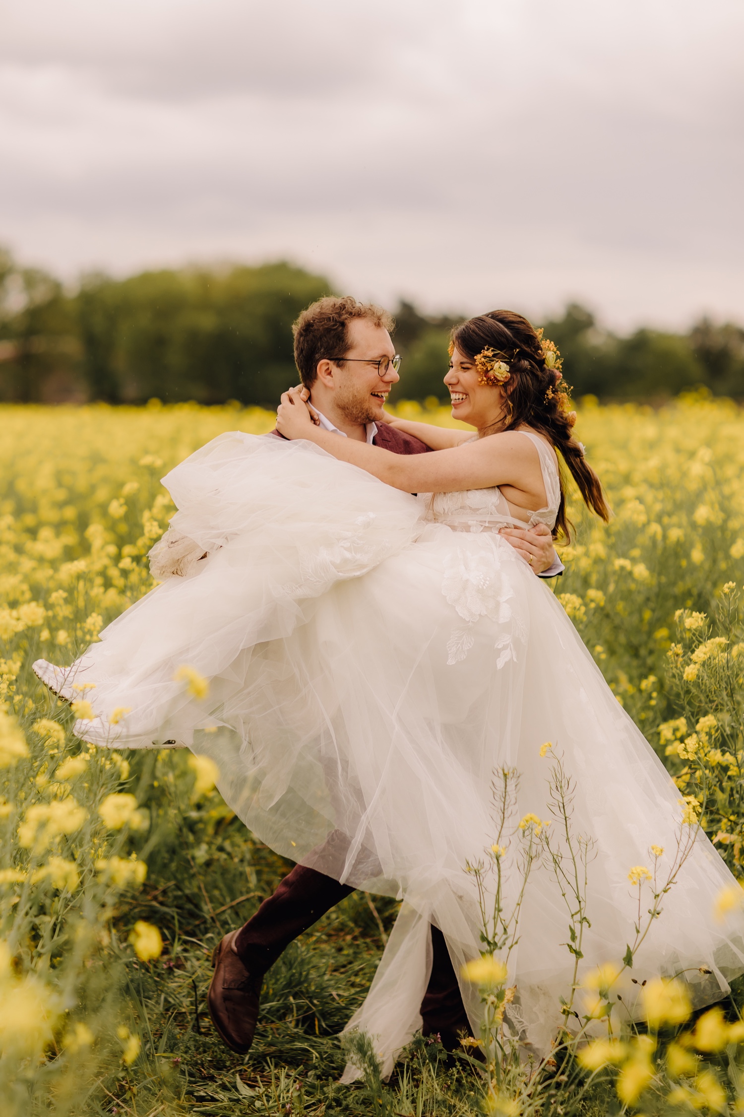 Huwelijksfotograaf Limburg - bruidegom zwiert met zijn bruid tussen de koolzaadbloemen