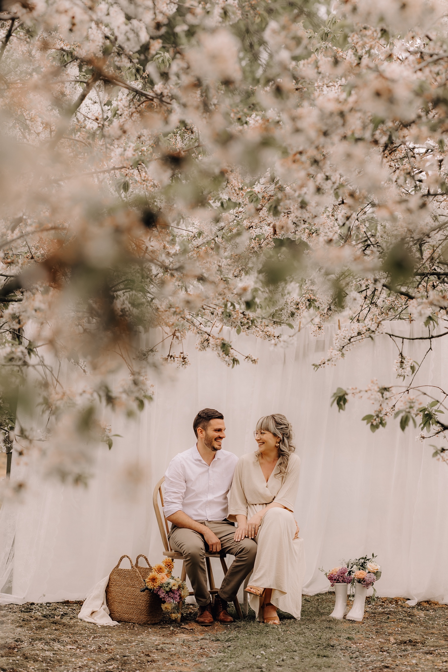 Huwelijksfotograaf Limburg - koppel poseert op stoel tussen de bloesems