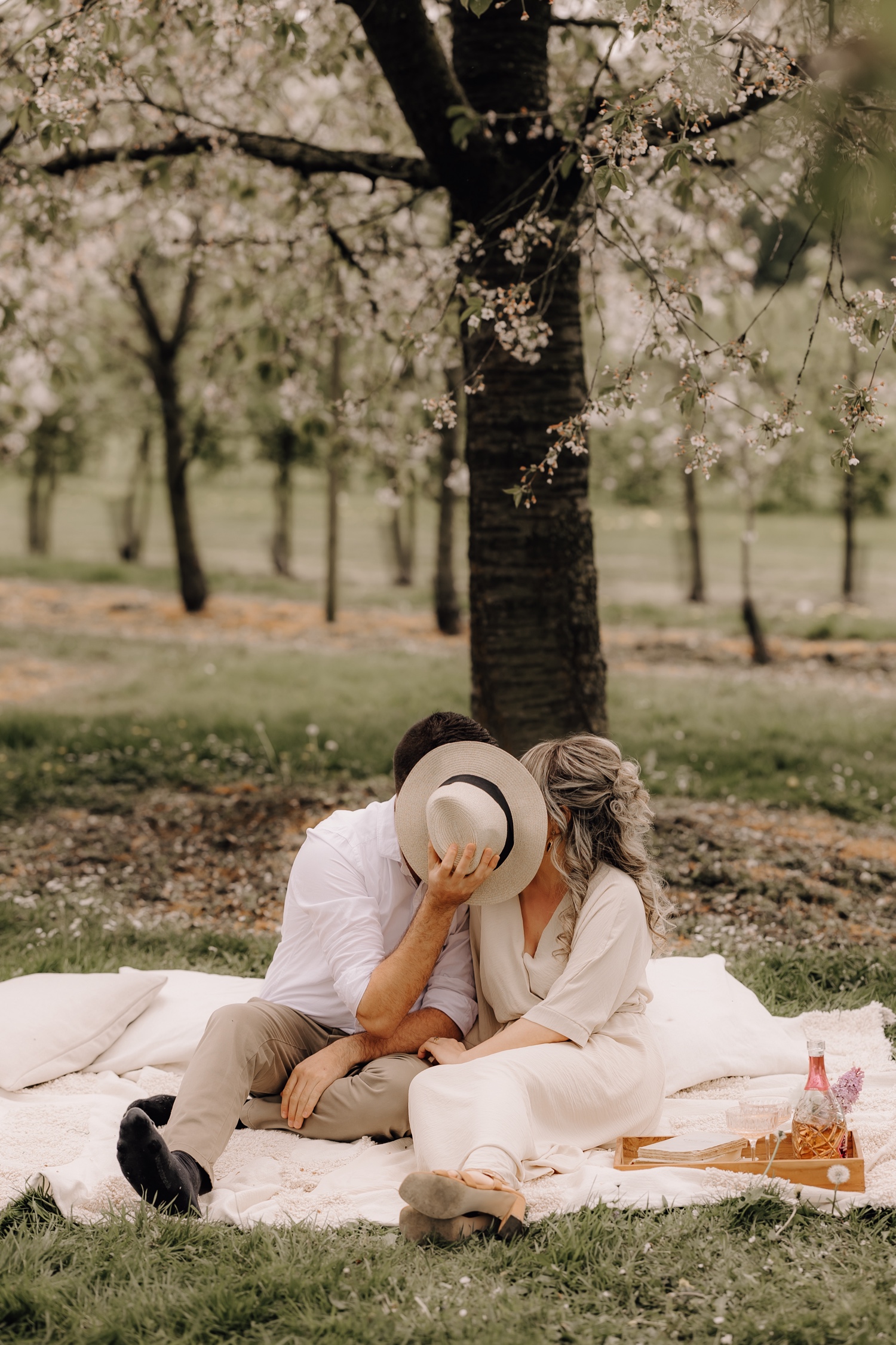 Huwelijksfotograaf Limburg - koppeltje kust achter een hoed tussen de bloesems