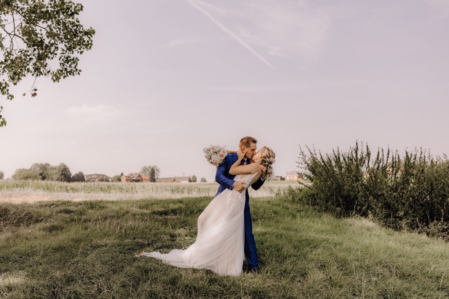 Zomers huwelijk op unieke landelijke locatie in Horebeke - bruidspaar kust elkaar innig tijdens fotoshoot in Horebeke