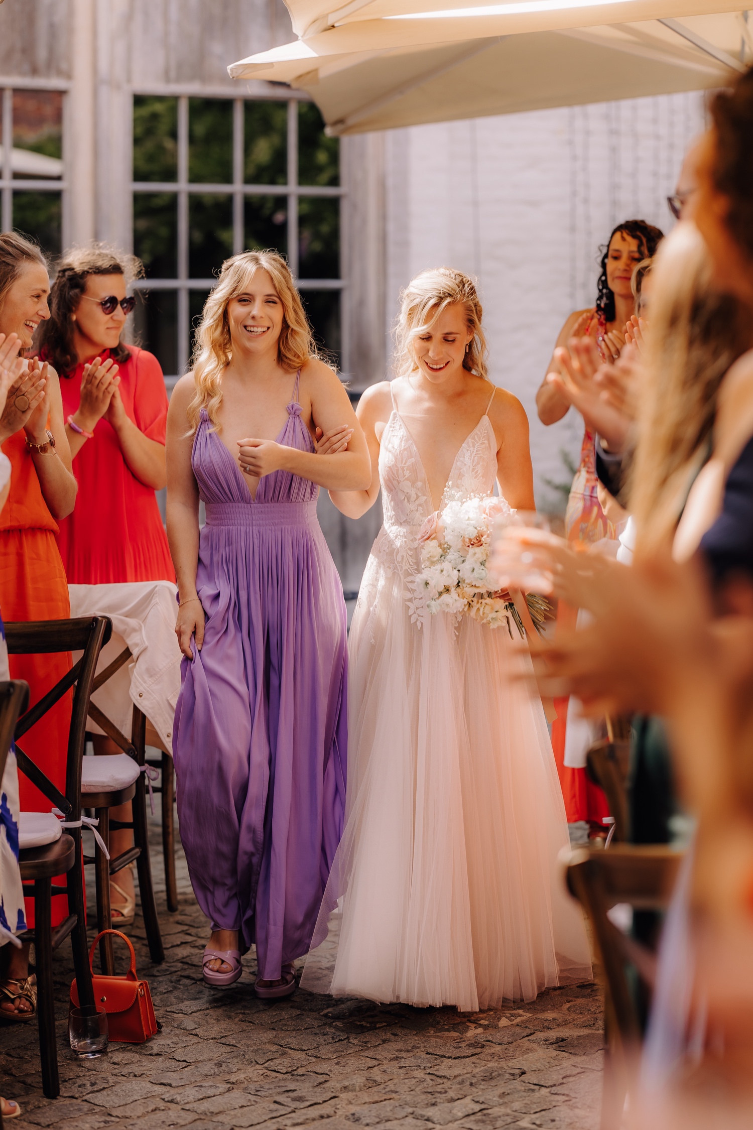 Zomers huwelijk op unieke landelijke locatie in Horebeke - bruid wandelt met haar tweelingzus door het gangpad van de ceremonie