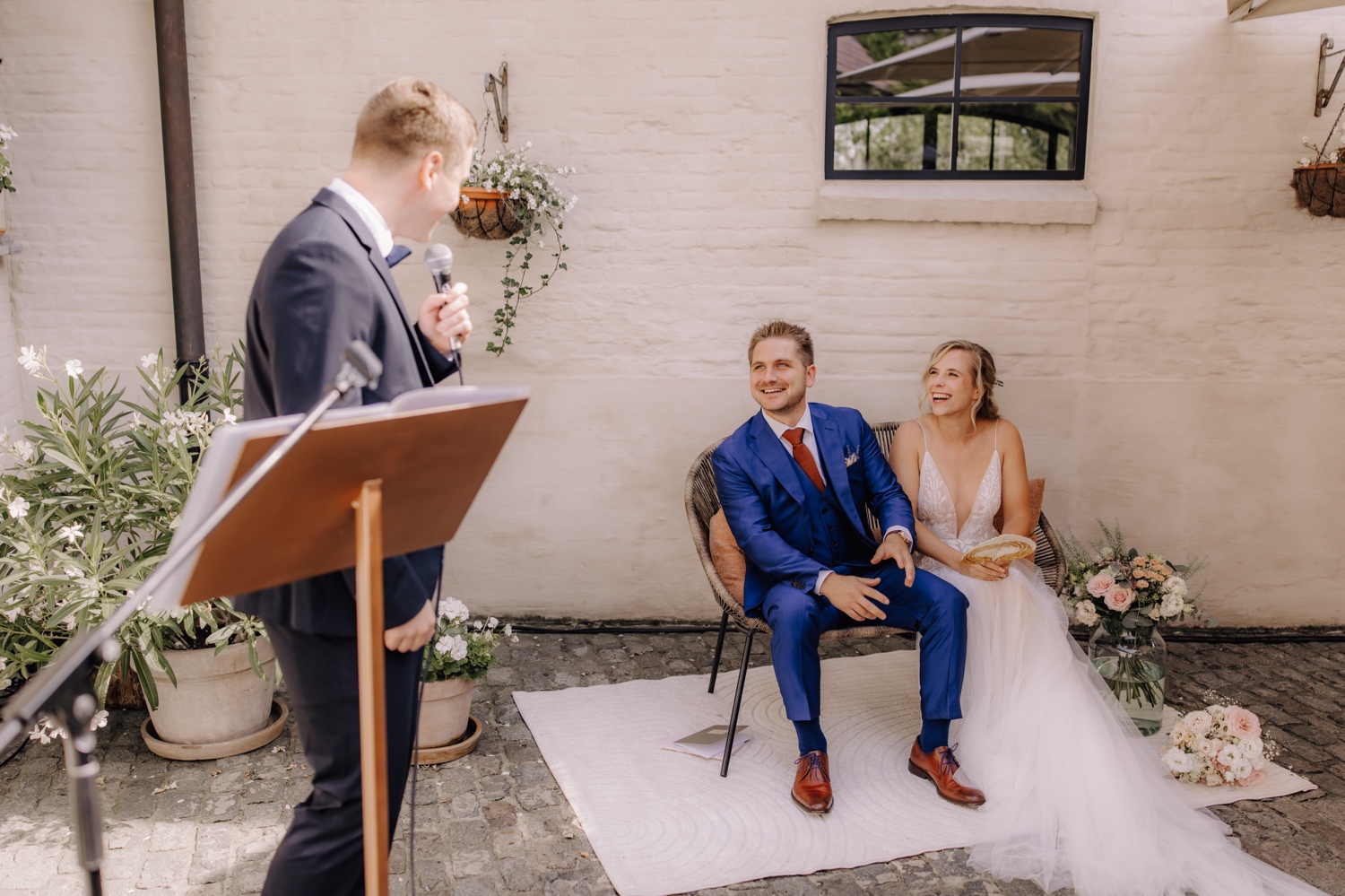 Zomers huwelijk op unieke landelijke locatie in Horebeke - bruidspaar lacht tijdens toespraak van de ceremoniemeester