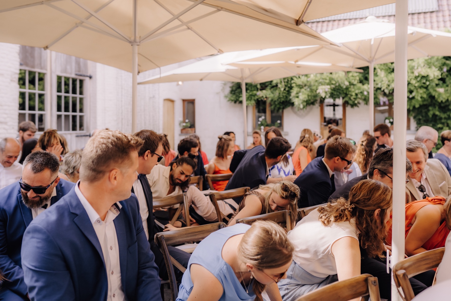 Zomers huwelijk op unieke landelijke locatie in Horebeke - gasten zoeken naar bruidsringen die willekeurig onder een stoel hangen