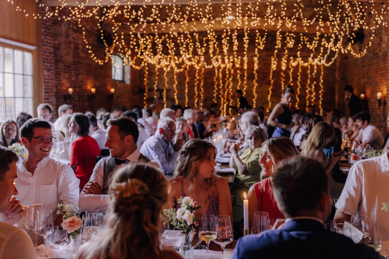 Zomers huwelijk op unieke landelijke locatie in Horebeke - overzichtsfoto van alle gasten aan tafel in de schuur