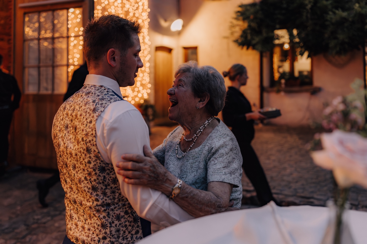 Zomers huwelijk op unieke landelijke locatie in Horebeke - oma omhelst de bruidegom tijdens diner