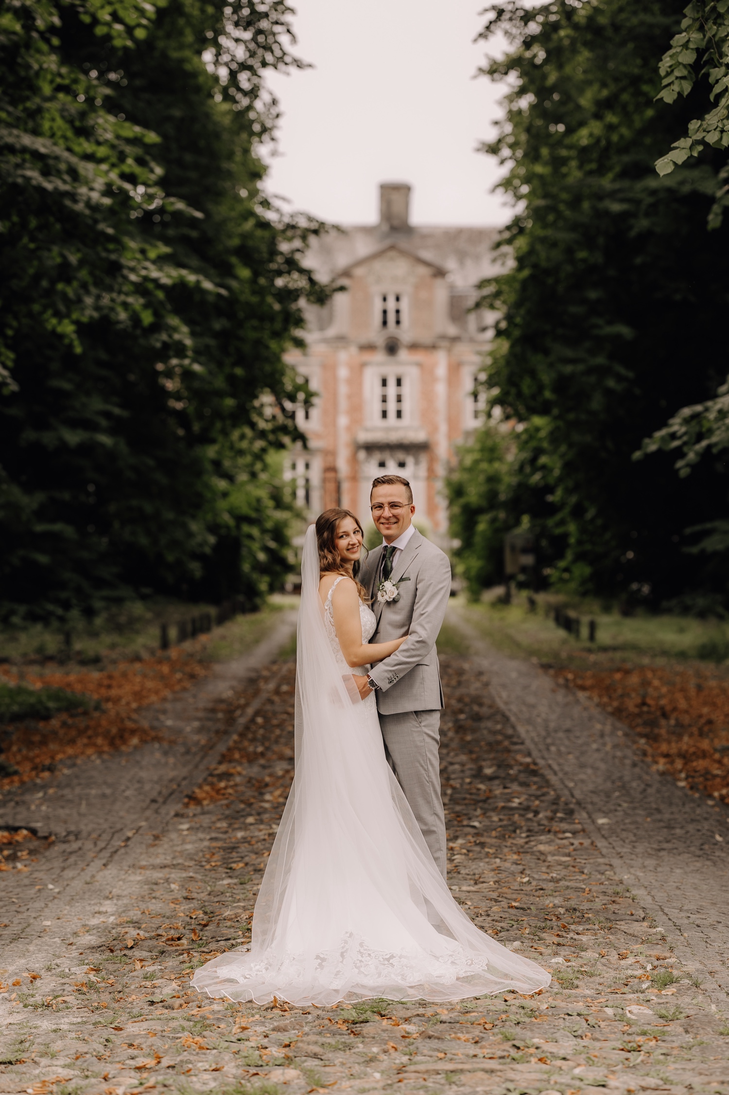 Intiem huwelijk bij La Butte Aux Bois - bruidspaar poseert in bomenlaan voor het Kasteel van Leut