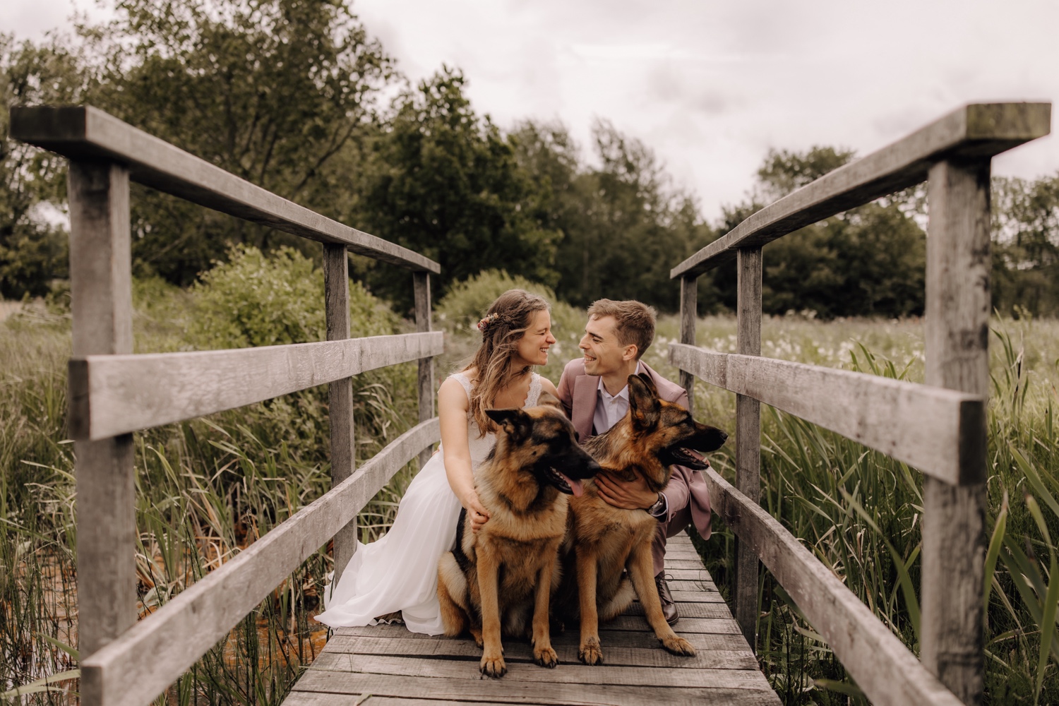 Een intiem huwelijk met twee honden en modderige laarzen - Bruidspaar poseert met hun twee Duitse herders op een vlonderpad in het Koersels natuurgebied