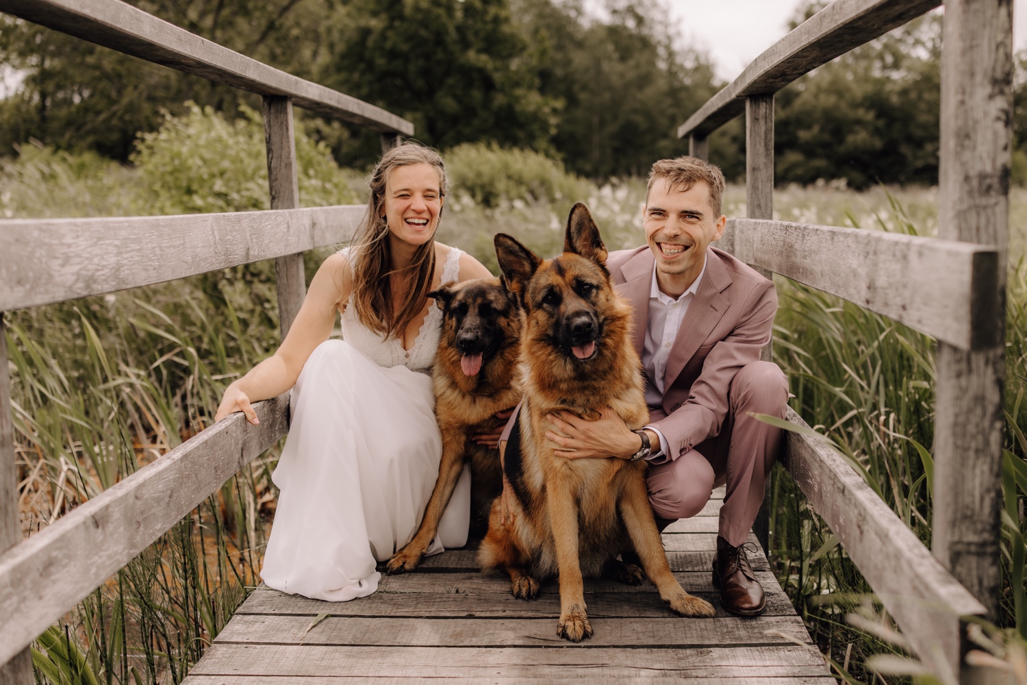 Een intiem huwelijk met twee honden en modderige laarzen - bruidspaar poseert met hun twee Duitse herders op een vlonderpad