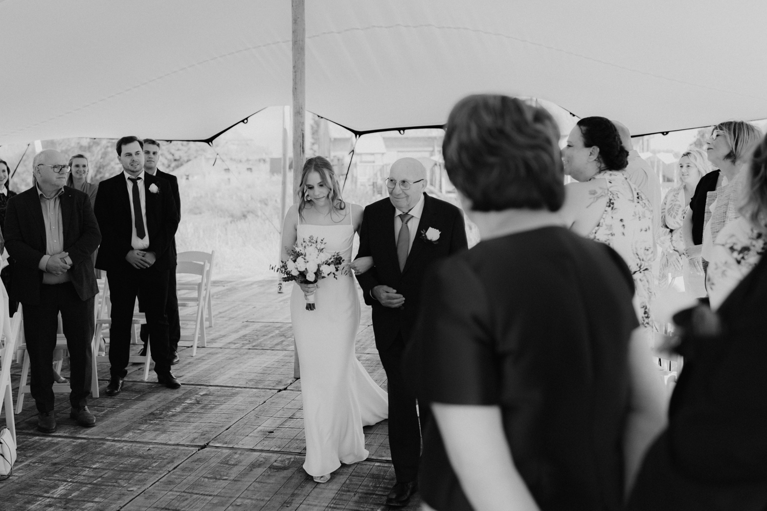 Landelijk huwelijk bij vierkantshoeve Bar Silo - Zwart-wit foto van de bruid die met haar grootvader door het gangpad van de ceremonie wandelt