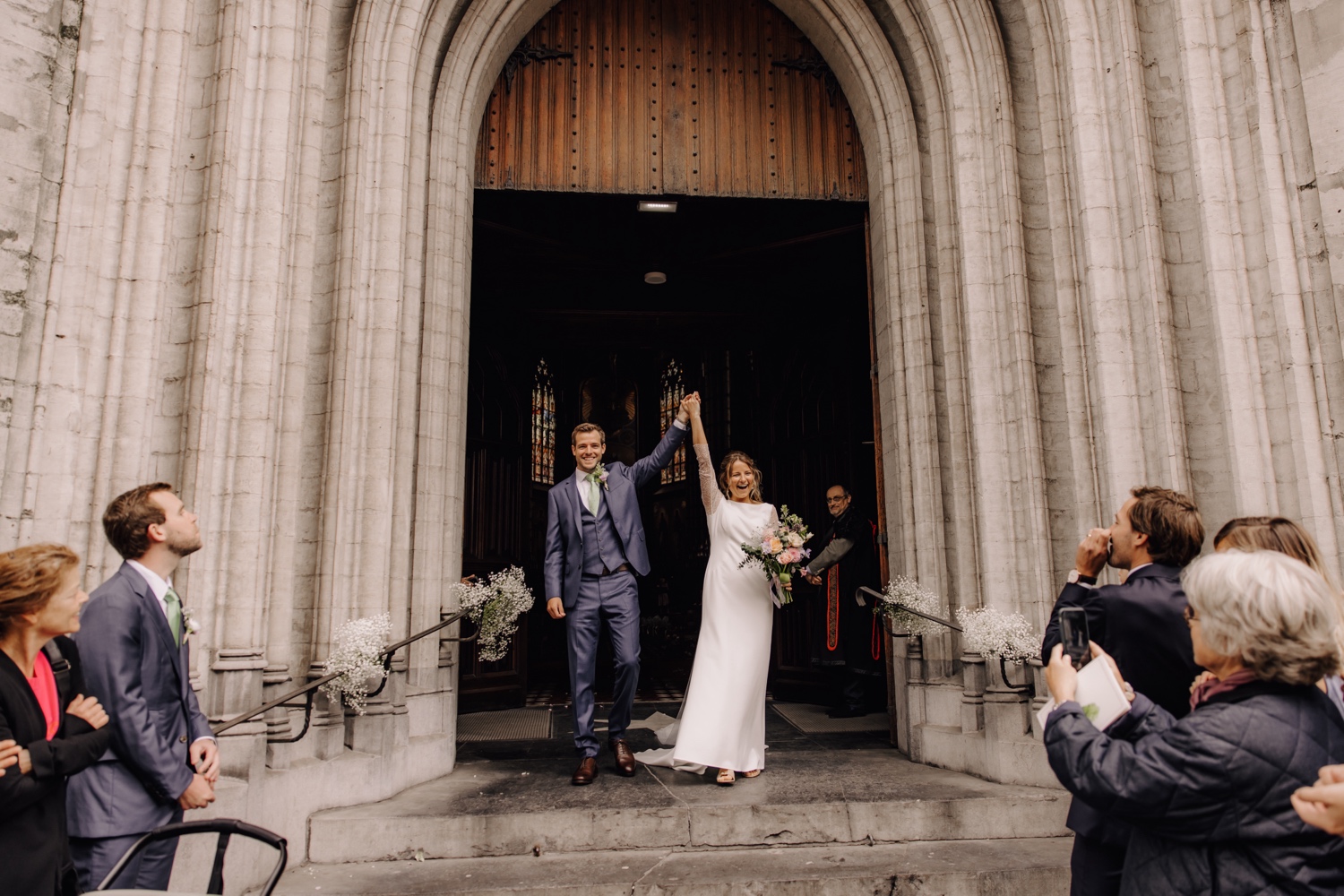 Een regenachtige huwelijksdag bij Hoeve Engelendael - bruidspaar juicht aan de poort van de kerk