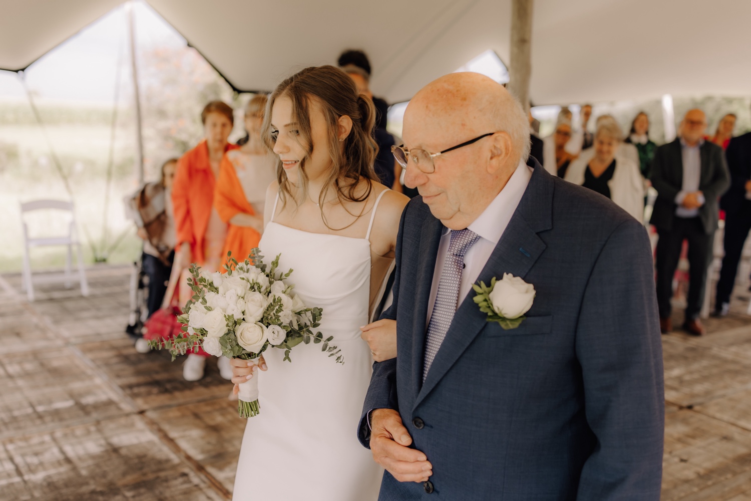 Landelijk huwelijk bij vierkantshoeve Bar Silo - bruid wandelt met haar grootvader door het gangpad van de ceremonie