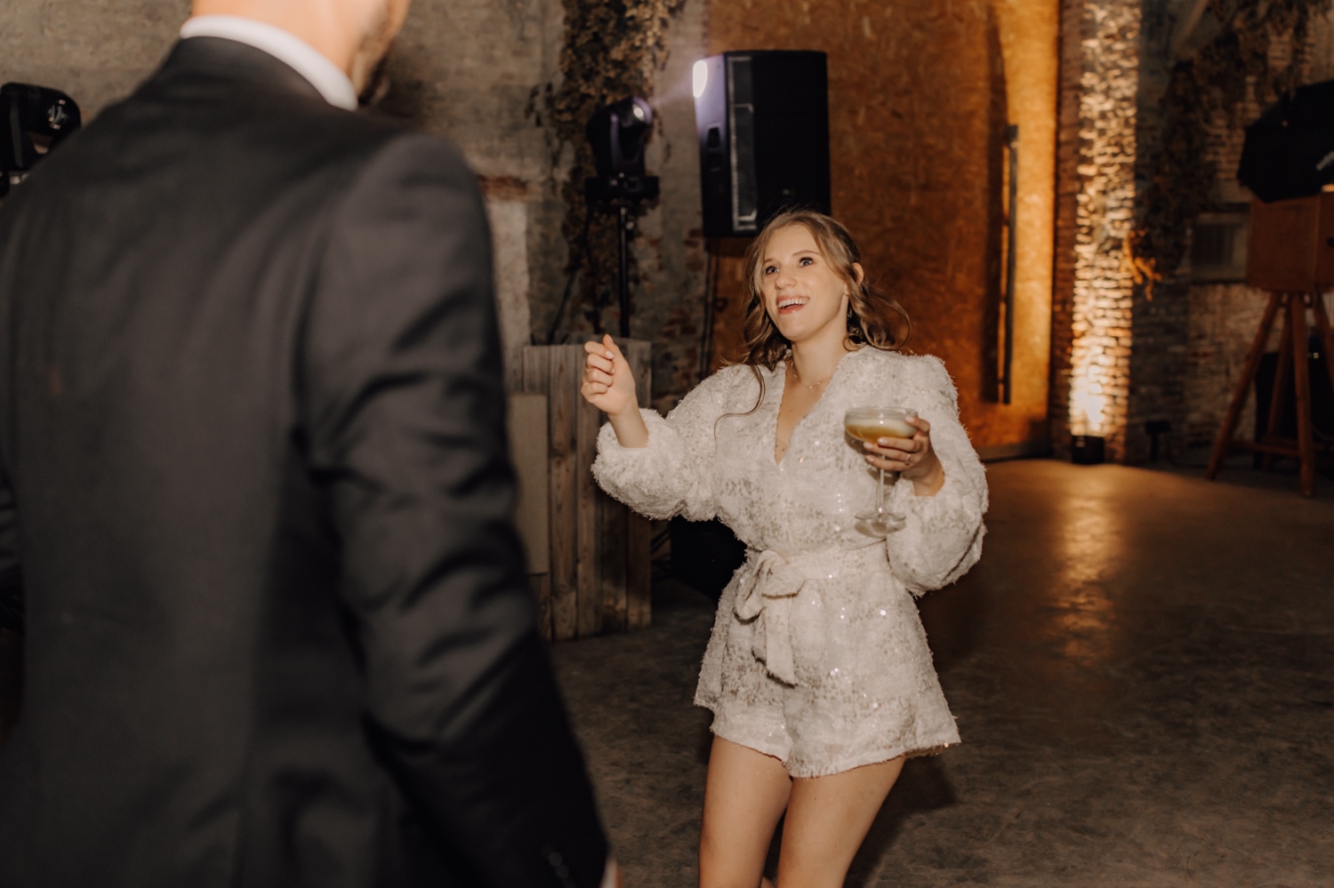 Landelijk huwelijk bij vierkantshoeve Bar Silo - bruid verschijnt in glitter playsuit op de dansvloer met een cocktail in de hand